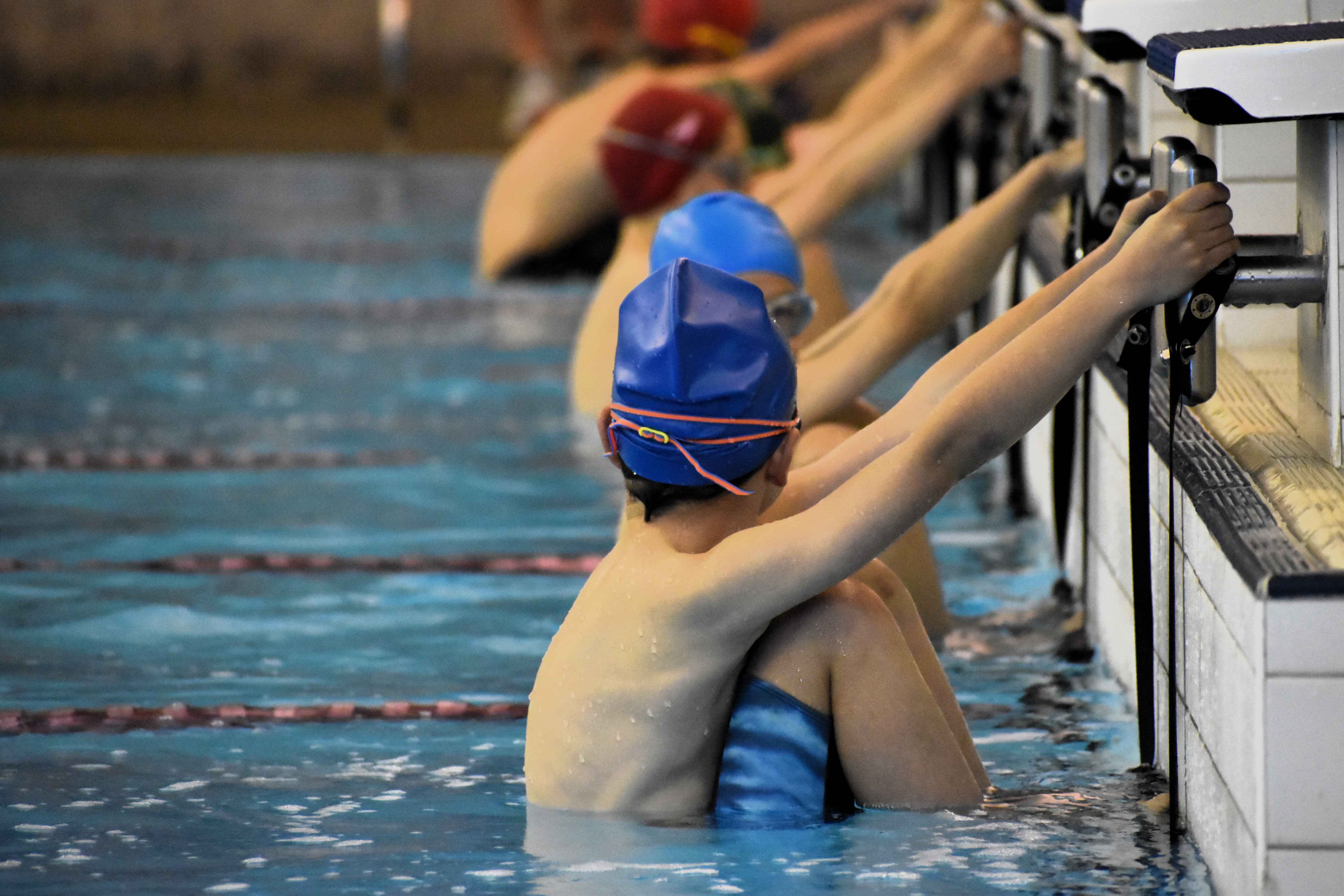 Action shot of male student swimmers in colourful caps ready for the backstroke start during a school swimming meet.