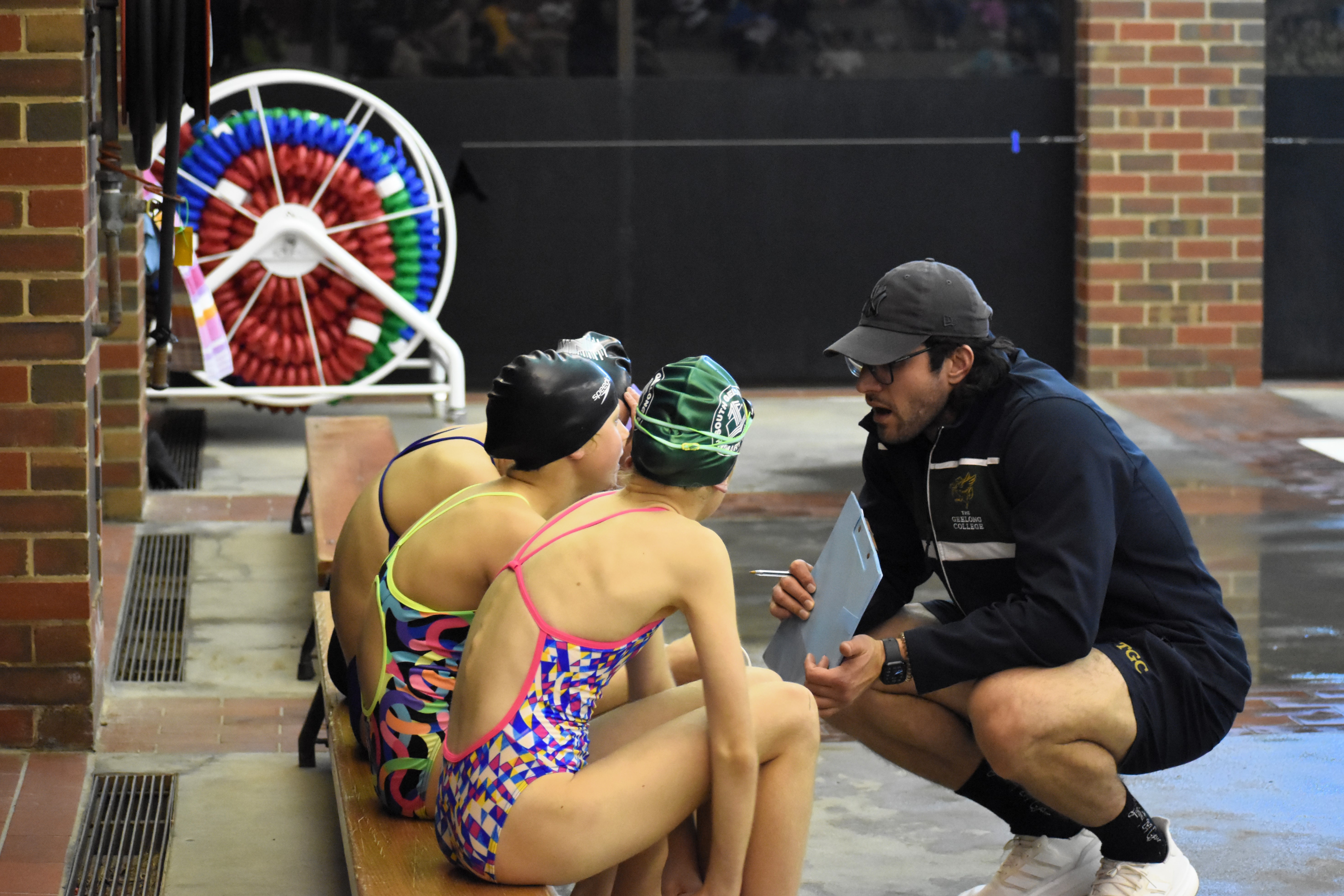 Female student swimmers in a team huddle with their coach, debriefing before their race at the school swimming competition.