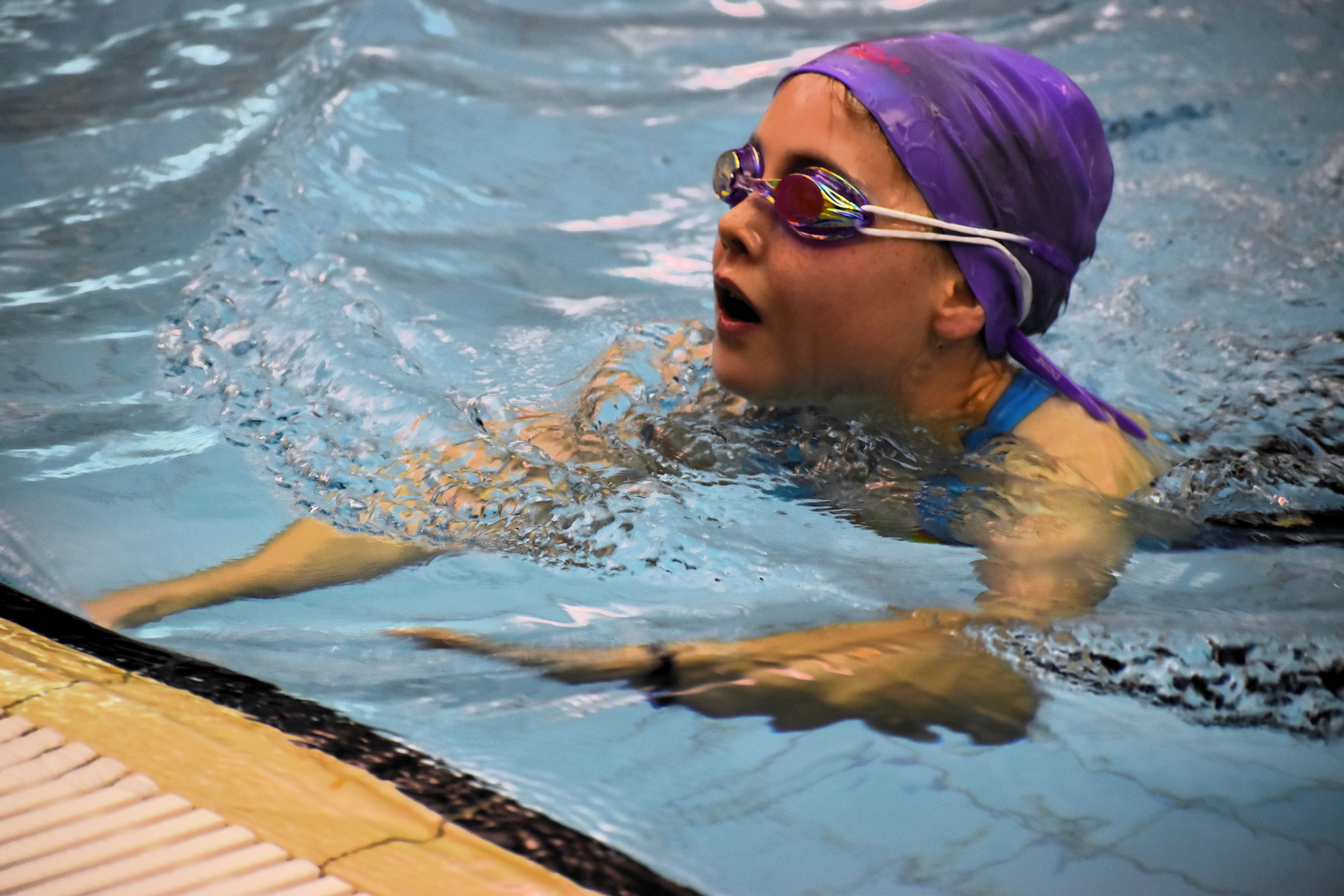 Female student swimmer reaching for the wall at the finish line of her race during a school swimming competition.