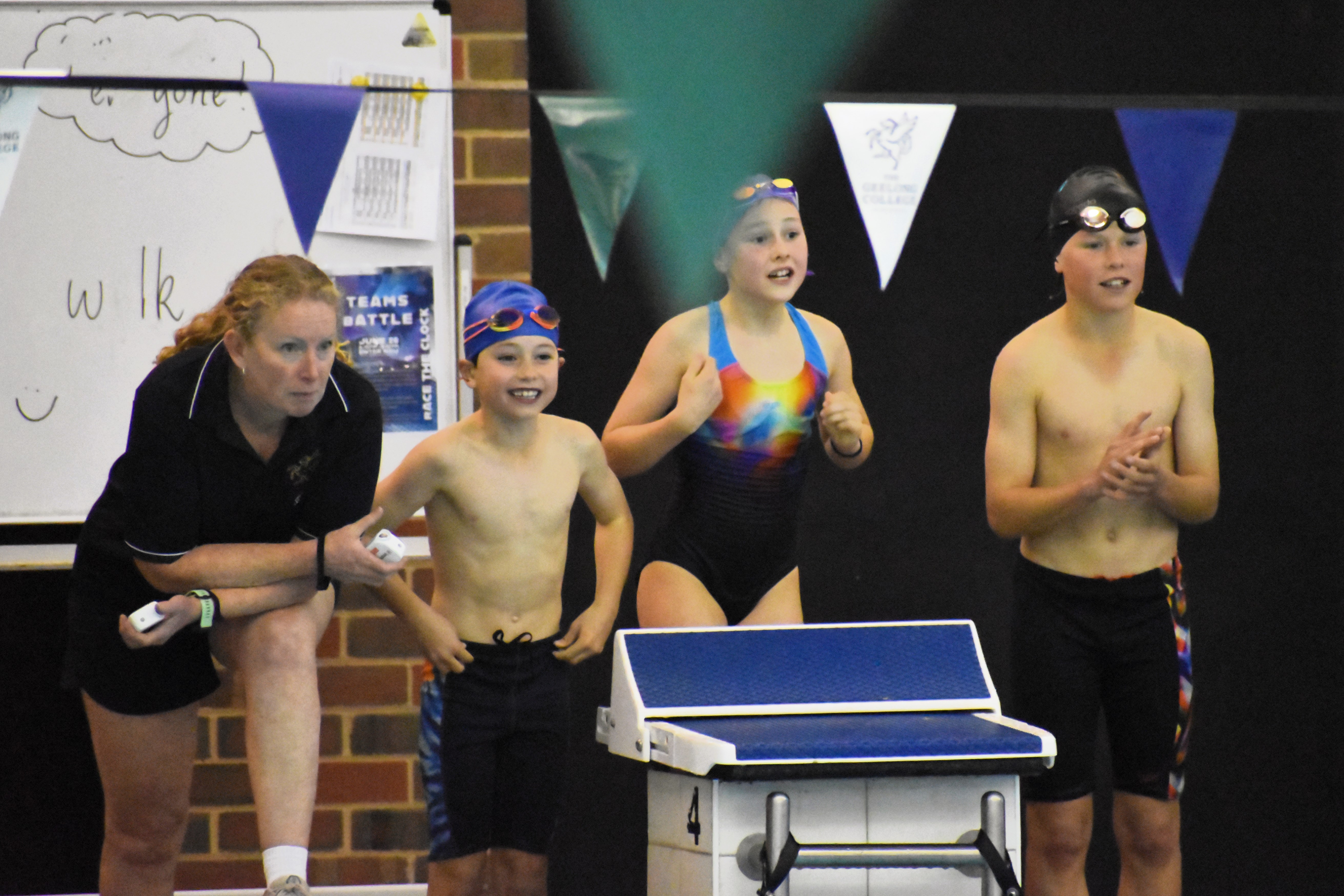 Student swimmers and their coach cheering on their teammates from the pool deck during the relay event.